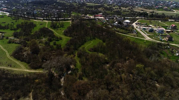 Létání nad ohromující městskou krajinou a zelenou letní krajinou. Zastřelen. Letecký pohled na zakřivené široké a úzké silnice a stezky a malé městečko v blízkosti hor. — Stock fotografie