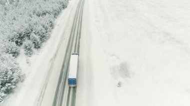 Karlı Ladin Ormanı 'ndan geçen boş bir yolda giden tomruk kamyonunun hava görüntüsü. Sahne. Ulaşım kavramı, kar boyunca hareket eden bir kamyon kış doğasını kapladı..