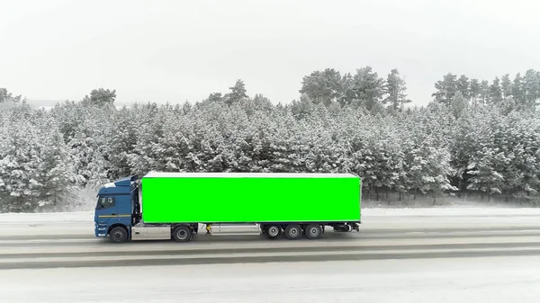 Widok z lotu ptaka na drogę w idyllicznym zimowym krajobrazie i ciężarówka z kluczem chroma zielone miejsce po stronie ciała. Scena. Pojęcie reklamy i transportu. — Zdjęcie stockowe