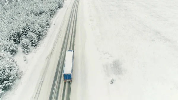 Vue aérienne d'un camion forestier circulant sur une route vide menant à travers une forêt d'épinettes enneigées. Scène. Concept de transport, un camion se déplaçant le long de la neige couverte nature hivernale. — Photo