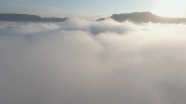 Bulutların üstünde dağların tepeleriyle güzel bir gökyüzü manzarası. Vuruldu. Yoğun bulutlar dağ tepelerine indi. Dağların zirvelerine yakın yoğun bulutların üzerinde şafak