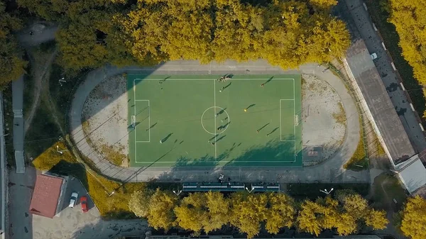 Aerial top view of football team practicing on a green soccer field. Video. Flying above an old sports stadium in a sleeping area of the city surrounded by trees and houses. — Stock Photo, Image