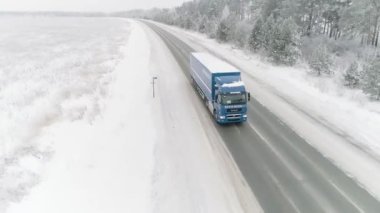 Cennet gibi kış manzarasında bir yol manzarası ve bir sürücü kamyonu. Sahne. Ulaşım kavramı, araba karla kaplı tarla ve kış ormanı boyunca hareket ediyor..