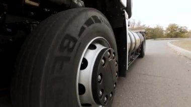  Kargo kamyonu boş otoyolda hızla gidip geliyor. Sahne. Bir yol ve ağaçların arka planında dönen araba tekerleğini kapat.