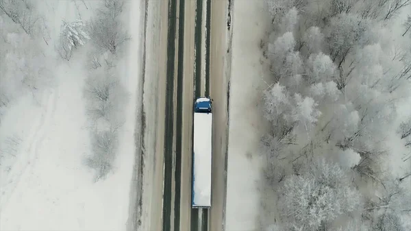 Widok z lotu ptaka na drogę przechodzącą przez zimowy las w ciężką pogodę. Scena. Widok z góry ciężarówki poruszającej się po prostej drodze otoczonej lasami pokrytymi śniegiem. — Zdjęcie stockowe