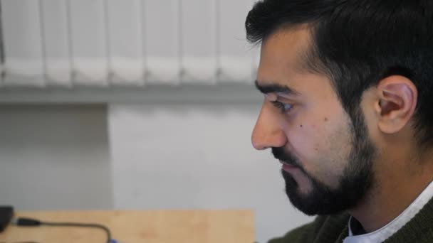 Zijaanzicht van een jonge, geconcentreerde man met een baard die werkt op een laptop. HDR. Kantoormedewerker zit aan zijn bureau en kijkt in het scherm. — Stockvideo