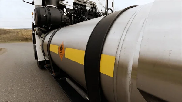 Caminhão-cisterna se move na estrada, perto do tanque de combustível de metal com um sinal de perigo de incêndio. Cena. Processo de transporte de petróleo dentro de um petroleiro moderno. — Fotografia de Stock