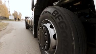 Otobandan geçen beyaz yük kamyonunu kapatın. Sahne. Kuru otoban asfaltında yuvarlanan kamyon tekerleği ve lastiğinin ayrıntılarına bak.