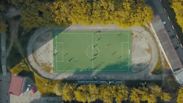 Vista aérea del equipo de fútbol practicando en un campo de fútbol verde. Vídeo. Volando por encima de un antiguo estadio deportivo en una zona de descanso de la ciudad rodeada de árboles y casas. — Vídeos de Stock
