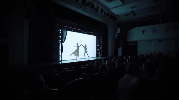 Σιλουέτες νεαρών ανδρών και γυναικών που εξασκούνται σε πιρουέτα κλασικού μπαλέτου στη σκηνή. Βίντεο. Σκοτεινή αίθουσα συναυλιών με κοινό βλέποντας μπαλέτο. — Αρχείο Βίντεο