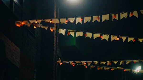 Μικρές σημαίες γιρλάντα, κινεζική διακόσμηση κατά το νυχτερινό ουρανό και το κτίριο. Βίντεο. Όμορφες σημαίες και φωτιστικά γιρλάντες κρέμονται στο σχοινί ένα προς ένα. — Φωτογραφία Αρχείου