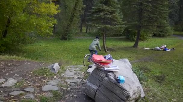 Łąka w lesie z pieszymi rzeczami leżącymi na zielonej trawie. Nagranie. Kobieta jeżdżąca rowerem po zielonych drzewach, koncepcja aktywnego stylu życia. — Wideo stockowe