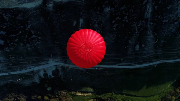 Vue aérienne du sommet d'une montgolfière rouge flottant au-dessus d'une pente de montagne, d'un sentier étroit et d'une prairie verte. Fusillade. Concept de voyage et d'aventure. — Photo