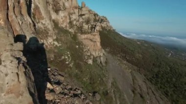 Uçurumun ve yaz ormanlarındaki dağlık alanlardaki kayaların havadan görünüşü. Vuruldu. Bir kaya eğiminin hava panoramik görüntüsü ve arka plandaki ağaçların üzerindeki bulutlar.