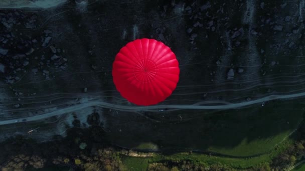 Bir dağ yamacında yüzen kırmızı sıcak hava balonunun, dar bir patikanın ve yeşil bir çayırın havadan görünüşü. Vuruldu. Seyahat ve macera kavramı. — Stok video