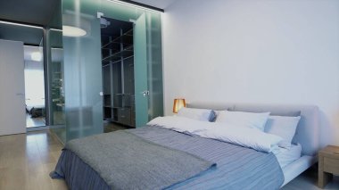 Yatak odası güneş ışığıyla dolu yeni bir otel odası. Video kaydı. Çift kişilik yatağı, lambası, komodini ve soyunma odası olan güzel bir yer..