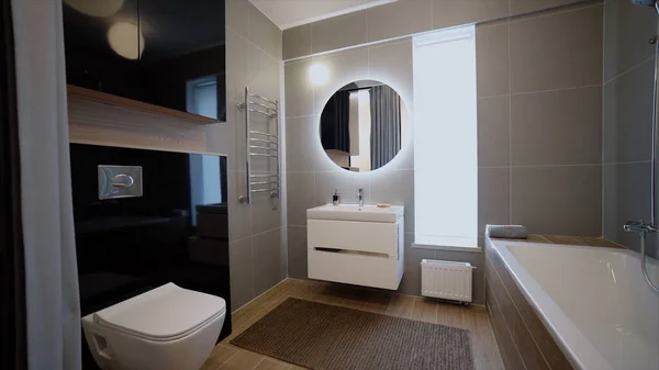 Modern fashionable residential bathroom interior inside new apartment. Video. View inside of a new flat after the repair, a toilet, a tub, mirror with illumination, and a cabinet with sink. — Stock Photo, Image