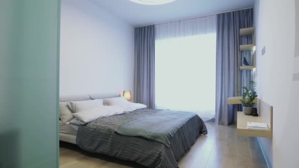Новый гостиничный номер со спальней, полной солнечного света. Видео. Интерьер с двуспальной кроватью, лампой, большим окном и полками на стене. — стоковое видео