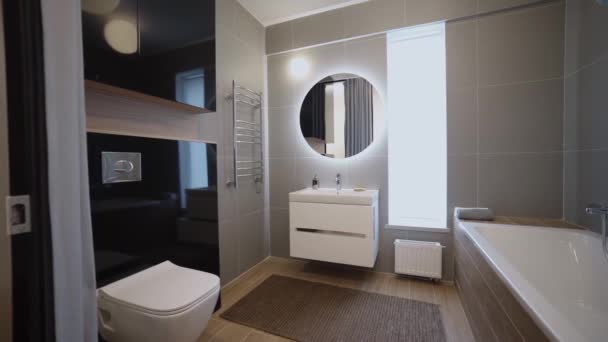 Modern fashionable residential bathroom interior inside new apartment. Video. View inside of a new flat after the repair, a toilet, a tub, mirror with illumination, and a cabinet with sink. — Stock Video