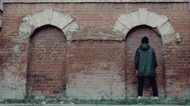 Bageste billede af en mand i sort tøj stående mod røde murstensvæg inde i en bue. Videoen. Ung mand hæve sine hænder og røre mursten bue. – Stock-video