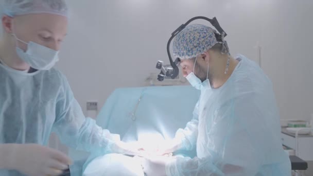 Два хірурги виконують операцію на людині. Дія. Хірурги професійно проводять операцію на пацієнта під анестезією. Світлова операційна кімната та хірурги, що виконують операцію — стокове відео