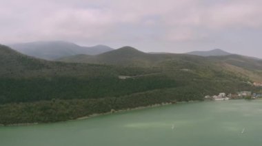 Yeşil dağları ve kıyıları olan bulutlu güzel manzaranın en üst manzarası. Başla. Yeşil dağlı yaz manzarası ve kasaba kıyısı yakınında su.