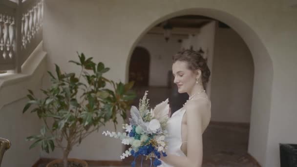 家で花束のポーズを持つ美しい花嫁。行動だ。エレガントなドレスの若い花嫁は手に花の花束で笑顔。美しい花嫁喜んでポーズのためにカメラ — ストック動画