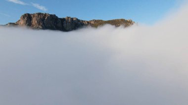 Yoğun bulutların üzerinden dağlara uçuyorlar. Vuruldu. Dik kayalık dağların yakınındaki kalın bulutların üst görüntüsü. Şafak vakti dağların yakınında güzel bulutlar