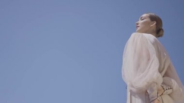 Gökyüzünün arka planında beyaz elbiseli güzel bir kadın. Başla. Mavi gökyüzünün arka planında şık elbiseler giymiş bir model. Açık havada, mavi gökyüzü olan zarif bir kadın.