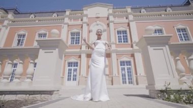 Eski binanın arka planında beyaz elbiseli zarif bir kadın. Başla. Saray arka planında zarif elbiseler içinde lüks bir gelin. Şık gelin, güneşli bir günde sarayda gülümser ve poz verir.