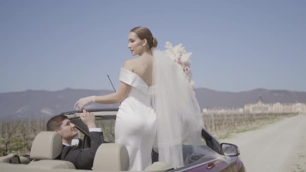 Hermosos recién casados en coche. Acción.Recién casados elegantes y carismáticos en coche. Apasionada sesión de fotos de recién casados en convertible. Dominante novia y marido en el amor en sesión de fotos con convertible — Vídeo de stock