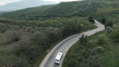 Dar bir bükme yolunda hareket halindeki aracın hava görüntüsü. Vuruldu. Yeşil vadiyle kırsalda güzel bir yaz günü.