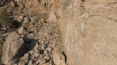 Hızlı uçuş dalışı, parlak güneşin altındaki kayalık yamaçlara yakın. Vuruldu. Yeşillikli doğal uçurumların havadan görünüşü.