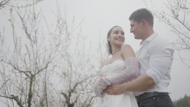 Newlyweds hug on background of sky. Action. Happy couple of newlyweds are gently embracing on background of overcast sky. Beautiful husband and wife are smiling happily in wedding dresses — Stock Video
