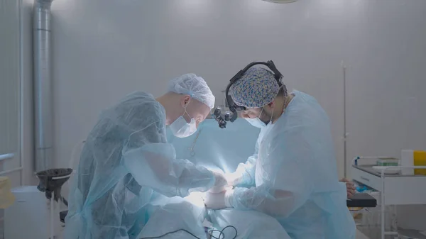 Két sebész műti meg az embert. Felvétel. A sebészek hivatásszerűen végeznek műtétet altatásban. Fényműtő és műtétet végző sebészek — Stock Fotó