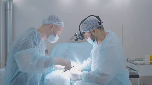 Két sebész műti meg az embert. Felvétel. A sebészek hivatásszerűen végeznek műtétet altatásban. Fényműtő és műtétet végző sebészek — Stock Fotó