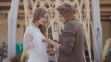 Hippi tarzında düğün. Başla. Yeni evliler taç takıp yüzüklerini takacak. Hippi yeni evliler örülmüş tacın arka planında güzel kıyafetler giyerler.