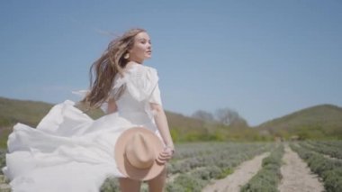Beyaz elbiseli güzel bir kadın tarlada koşuyor. Başla. Kadın saçı ve elbisesi koşarken çok güzel çırpınıyor. Beyaz uzun elbiseli bir kadının tarlada koşması ağır çekimde
