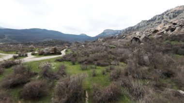 Dağların eteklerinde kayalar genişliyor. Vuruldu. Taşlarla, yeşilliklerle kaplı ve bulutlu arka planda dar yollarla kesişen vahşi bir vadinin havadan görünüşü..