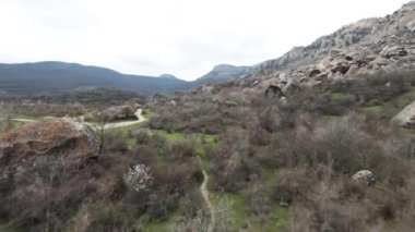 Dağların eteklerinde kayalar genişliyor. Vuruldu. Taşlarla, yeşilliklerle kaplı ve bulutlu arka planda dar yollarla kesişen vahşi bir vadinin havadan görünüşü..