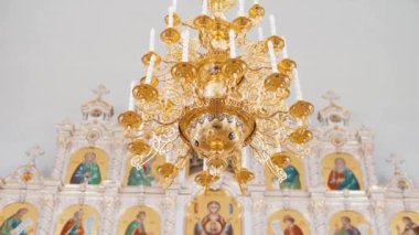 Hıristiyan ortodoks kilisesinin içi beyaz ve altın renklerle kaplıdır. Video kaydı. Tapınağın içinde ikonostaz mumları olan bir avize..