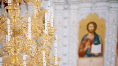 Hıristiyan ortodoks kilisesinin içi beyaz ve altın renklerle kaplıdır. Video kaydı. Tapınağın içinde ikonostaz mumları olan bir avize..