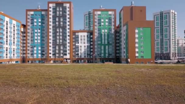 新しい近代的な、カラフルで、高層ビルと住宅地の空中ビュー。ビデオだ。建築の概念は、明るい青空の背景に新しい家や緑の牧草地に沿って飛んで. — ストック動画