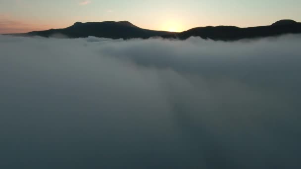 Vista aérea de un hermoso amanecer sobre montañas y espesa niebla. Le dispararon. Increíble vuelo sobre nubes blancas hacia la cordillera. — Vídeos de Stock