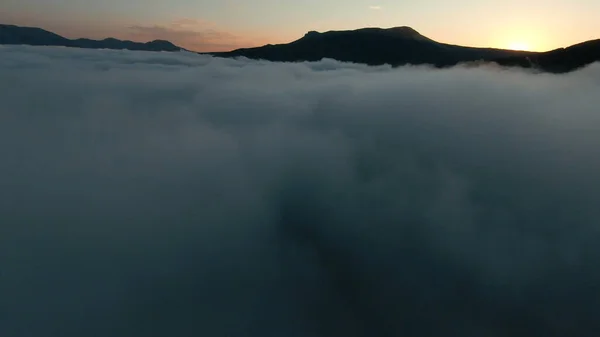 Vista aérea de un hermoso amanecer sobre montañas y espesa niebla. Le dispararon. Increíble vuelo sobre nubes blancas hacia la cordillera. — Foto de Stock