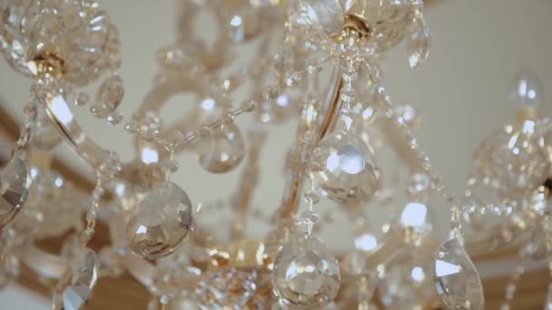 Elegant luxury chandelier with crystal on the ceiling inside a building. Video. Bottom view of a golden chandelier with rhinestones, interior details. — Stock Video