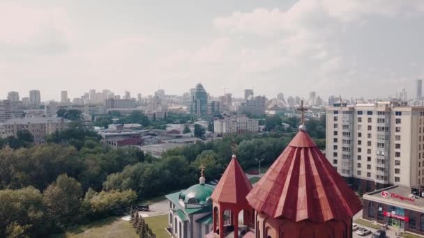 Flygfoto av en kyrka torn toppen av röda plattor med ett gyllene kors. Videon. Detaljer om en röd tegelbyggnad med en stad och molnig himmel på bakgrunden. — Stockvideo
