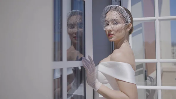 La novia elegante posa en la ventana. Acción. La novia posa en la imagen de boda de estilo en la terraza. Hermosa novia en vestido elegante se levanta en la ventana en el día soleado —  Fotos de Stock