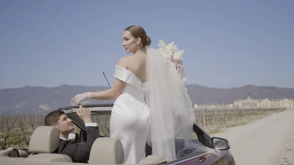 Beautiful newlyweds in car. Action.Stylish and charismatic newlyweds in car. Passionate photo shoot of newlyweds in convertible. Domineering bride and husband in love at photo shoot with convertible — Stock Photo, Image