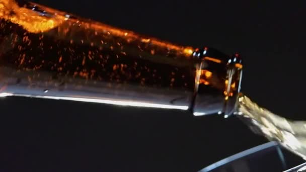 Close-up de derramar cerveja da garrafa marrom de vidro no copo. Vídeo. Derramando bebida alcoólica isolada em fundo preto, conceito de festa. — Vídeo de Stock